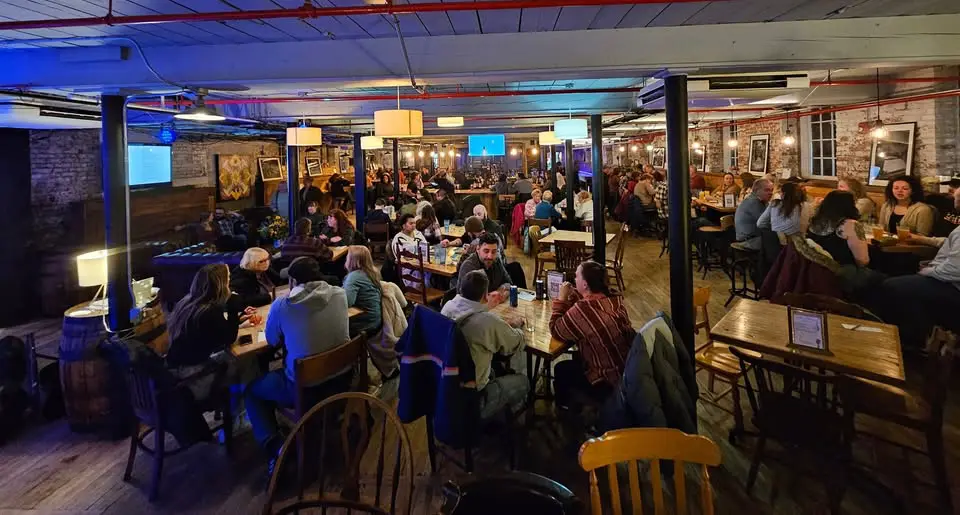 Crowded indoor restaurant with many people dining and socializing under warm lighting.