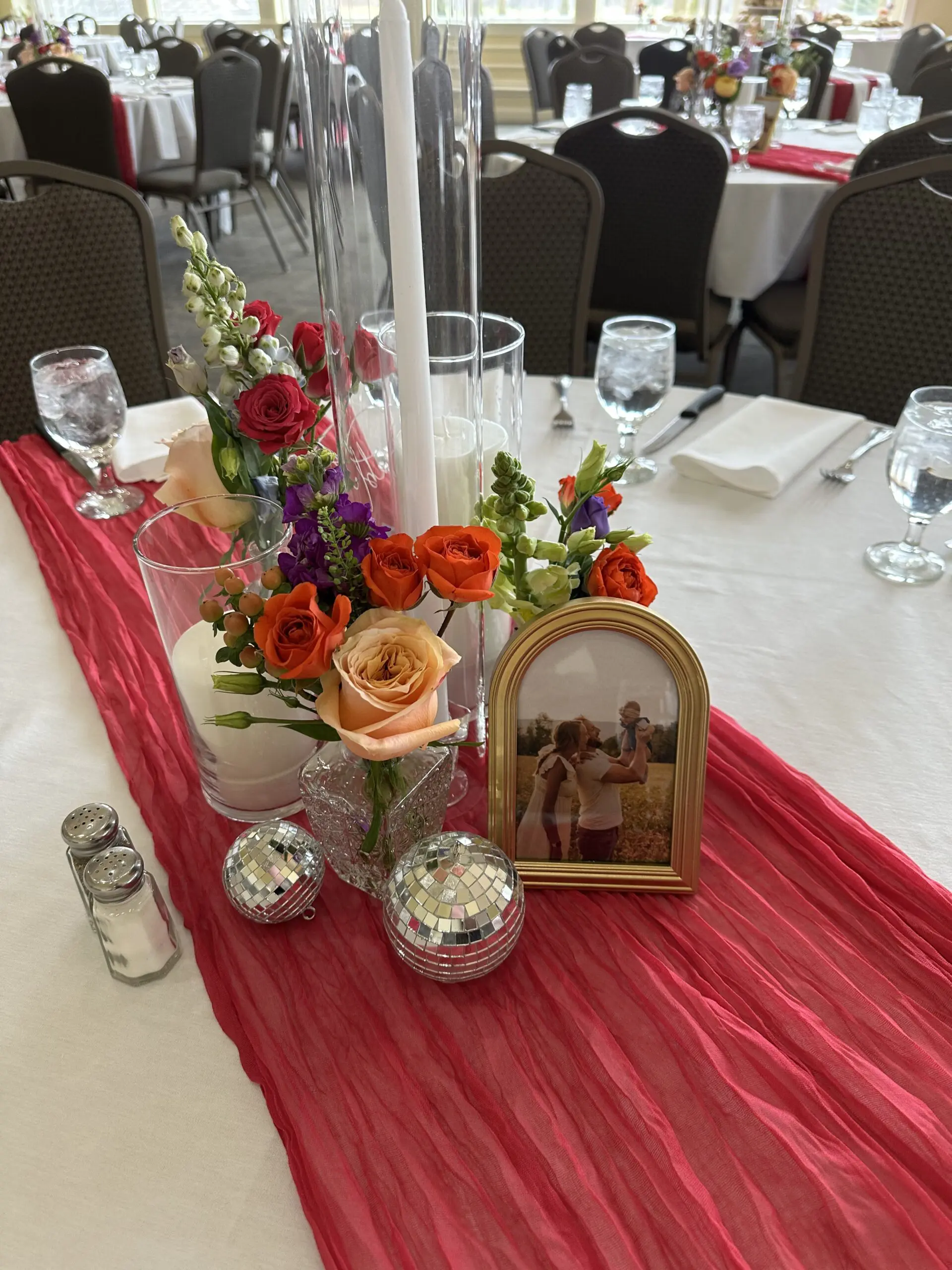 Elegant table centerpiece with flowers and candles on red runner.