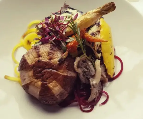 Gourmet roasted meat with grilled lemon and vegetable garnish.