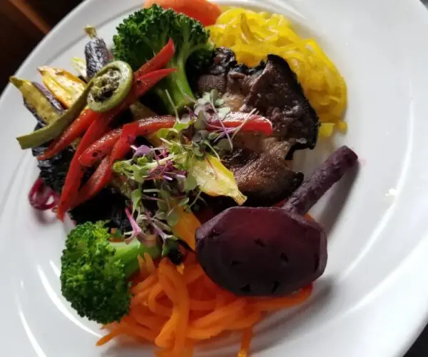 A colorful plate of grilled meat with vegetables and mashed potatoes.