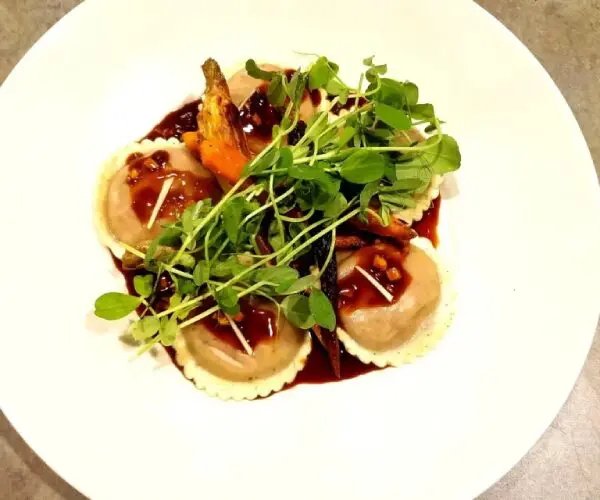 Seared scallops garnished with microgreens and a dark sauce.