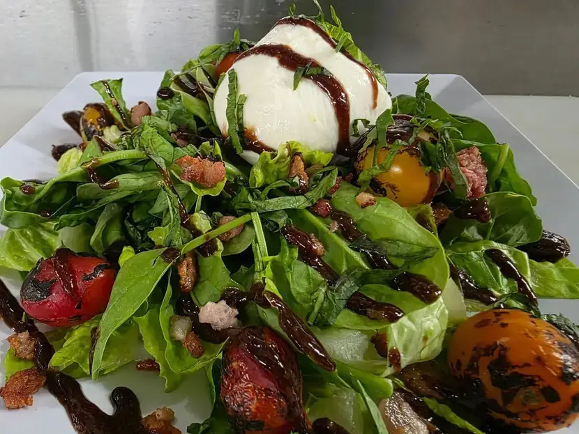 Fresh salad with greens, cherry tomatoes, and burrata cheese drizzled with balsamic glaze.