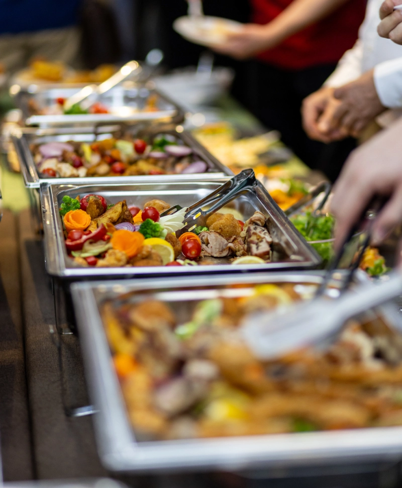A buffet line with various colorful dishes and people serving themselves.